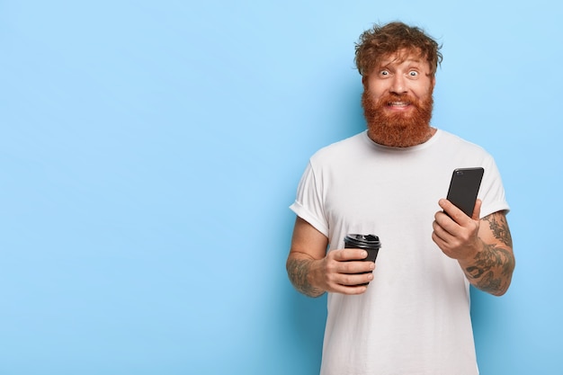 Free photo cheerful red haired guy posing with his phone