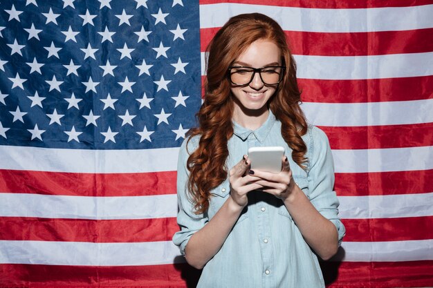 Cheerful redhead young lady standing over USA flag chatting