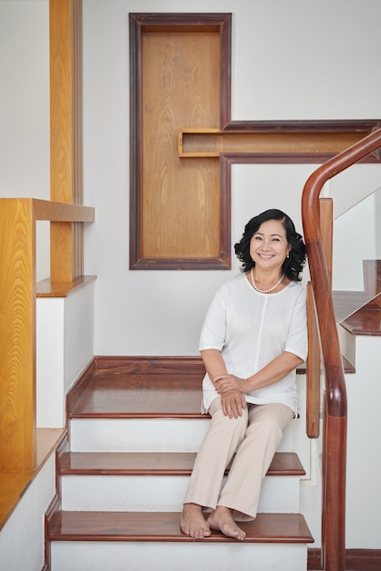 Free photo cheerful senior asian woman sitting on stairs at home