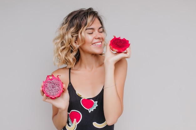 Free photo cheerful short-haired girl looking at juicy pitaya. indoor photo of spectacular tanned woman isolated with dragon fruit.