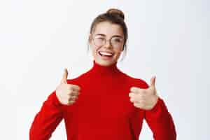 Free photo cheerful smiling female student in glasses showing thumbs up in approval, praise and recommend good thing, approve and like it, standing on white