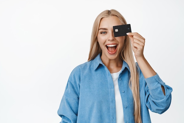 Cheerful smiling woman holding credit card against eye screaming happy standing over white background