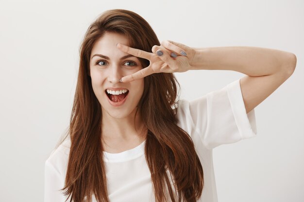 Cheerful smiling woman showing kawaii peace sign over eye