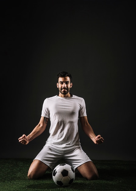 Free photo cheerful soccer layer sitting near ball