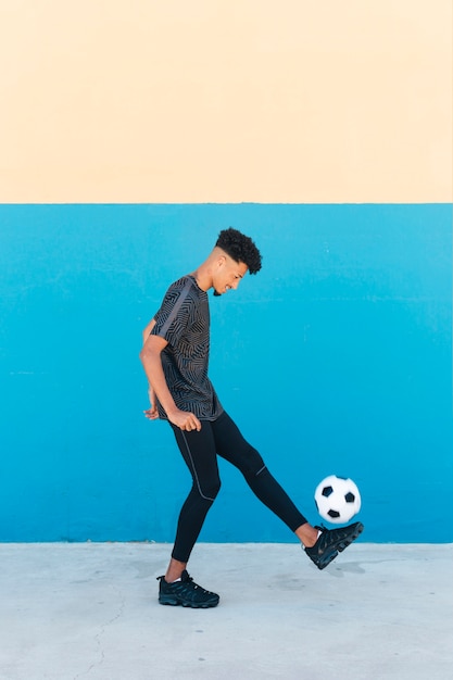 Cheerful sportsman kicking soccer ball near wall