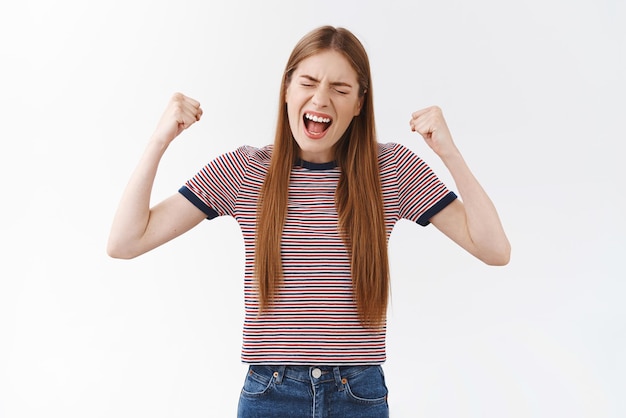 Free photo cheerful successful goodlooking girl in striped tshirt made dreams come true finally achieve goal fist pump raising hands in triumph yelling delighted accomplish victory feeling like champion