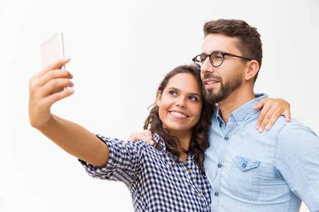 Cheerful sweet hugging and taking selfie on cellphone