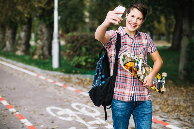 Cheerful teenager taking selfie with skateboard