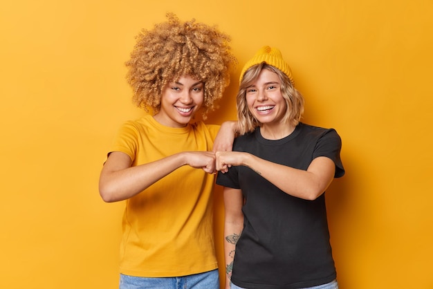 Free photo cheerful two young women make fist bump agree to work as team dressed in casual outfit smile gladfully isolated over vivid yellow background female partners enjoy teamwork celebrate achievement