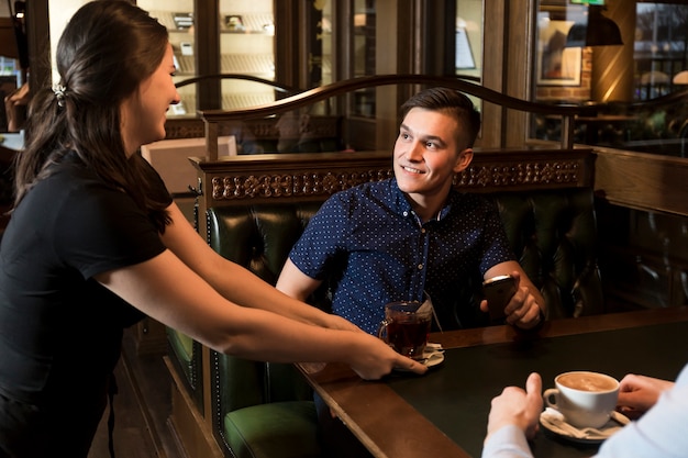 Cheerful waitress serving tea to handsome man