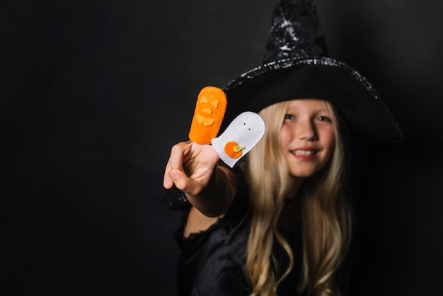 Free photo cheerful witch gesturing victory with halloween toys