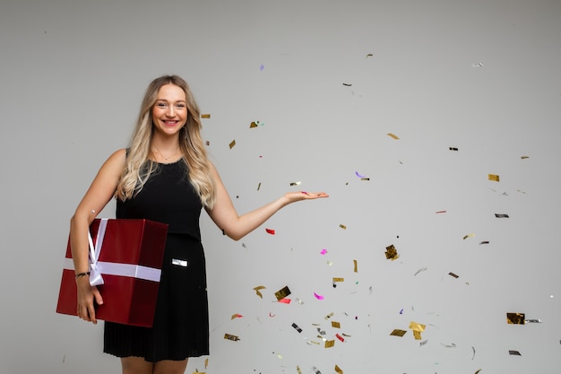 Cheerful woman in black dress rejoices of box with her christmas present with a lot of confetti around her