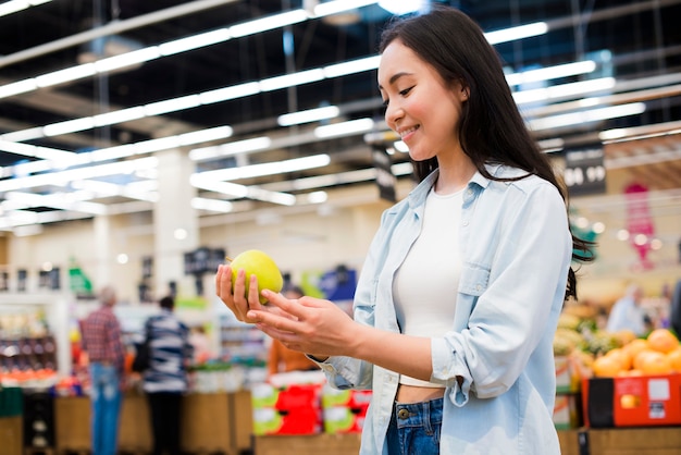 Free photo cheerful woman checking apple in grocery store