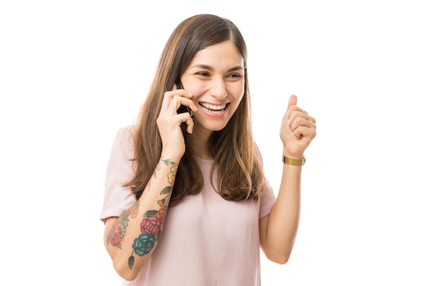 Cheerful woman clenching fist while talking on mobile phone against white background