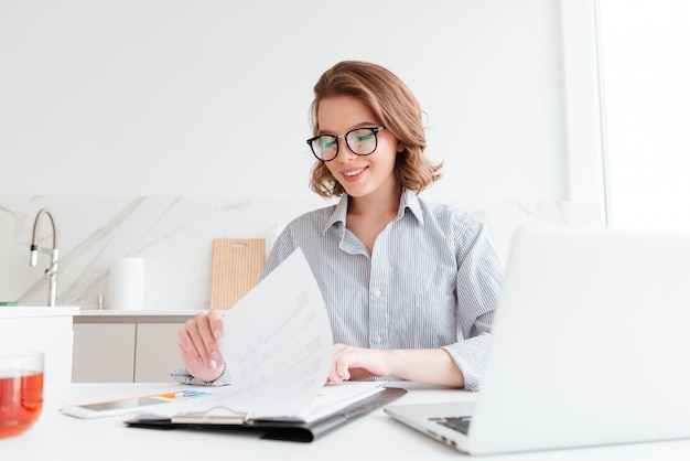 Free photo cheerful woman in glasses reading new contract while working in the kitchen