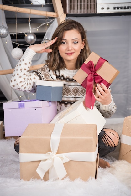 Cheerful woman holding a Christmas gift in living room. H