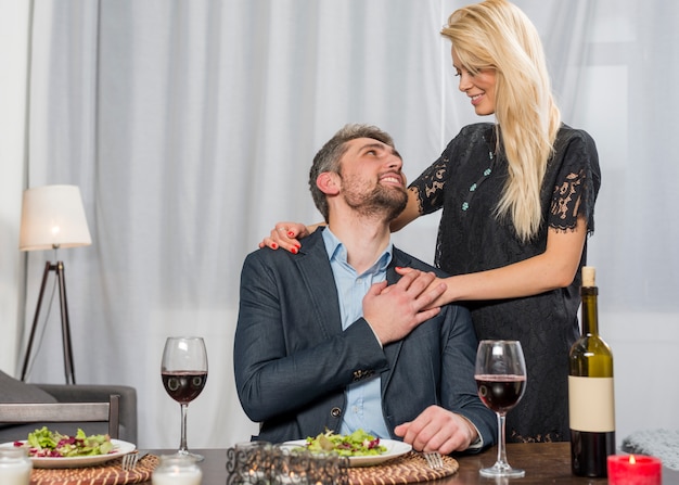 Cheerful woman hugging man at table with plates and glasses