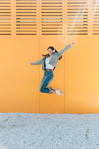 Free Photo cheerful woman jumping against wall outstretching her arms