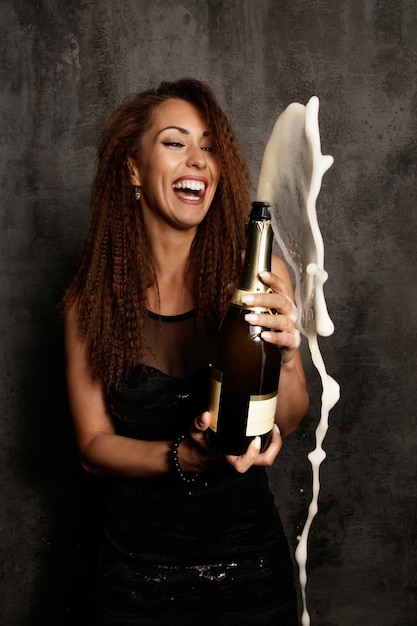 Cheerful woman opening bottle of Champagne and having fun at the party