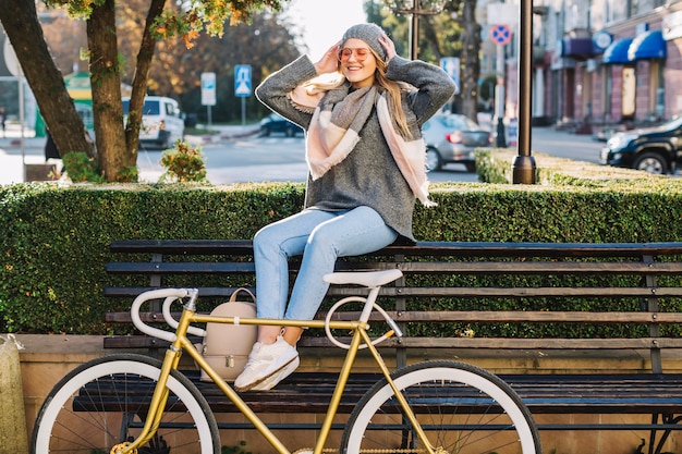 Cheerful woman sitting on bench near bicycle