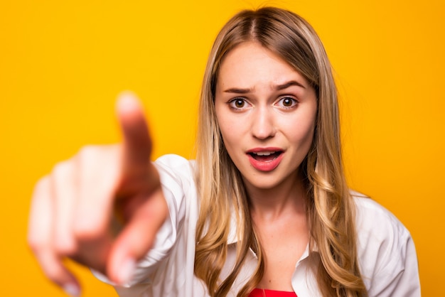 Cheerful woman in t-shirt pointing  with open mouth over yellow wall