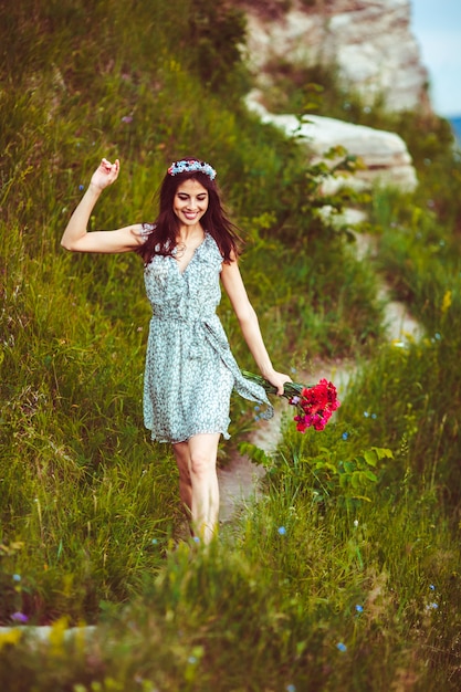 Free photo cheerful woman walks with red bouquet arond green hill