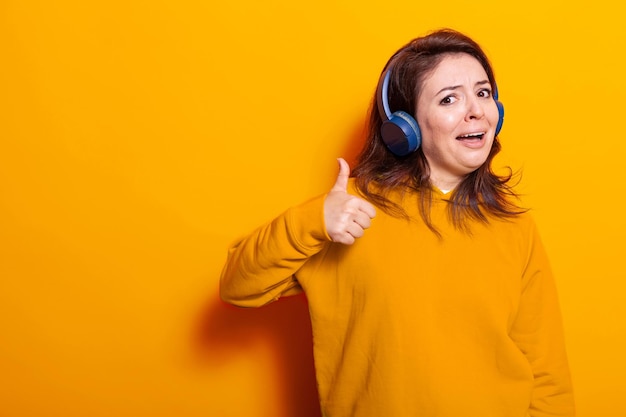 Free Photo cheerful woman wearing headphones to listen to music and showing okay symbol with hand on camera. positive adult feeling happy and listening to song and sounds on headset, having fun