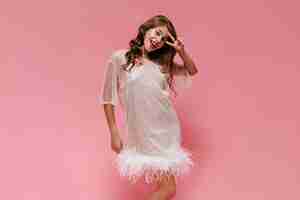 Free photo cheerful woman in white dress smiles widely on pink wall