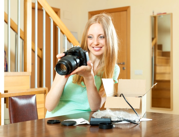 cheerful woman with blond hair unpacking for new digital camera at home