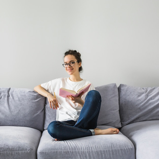 Cheerful woman with book on sofa