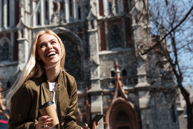 Free photo cheerful woman with cup of coffee and smartphone laughing