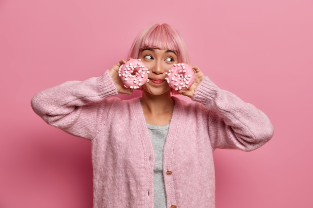 Free Photo cheerful woman with pink hairstyle, holds two glazed donuts, poses 