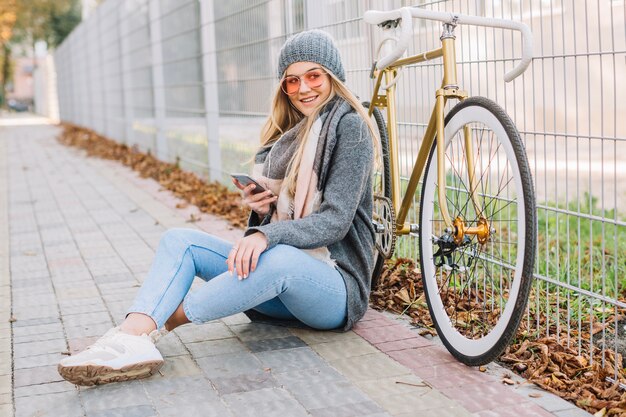 Cheerful woman with smartphone on pavement