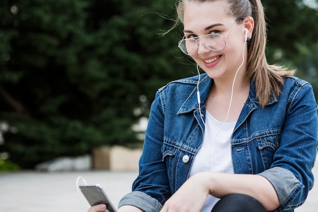 Free photo cheerful woman with smartphone sitting on sidewalk