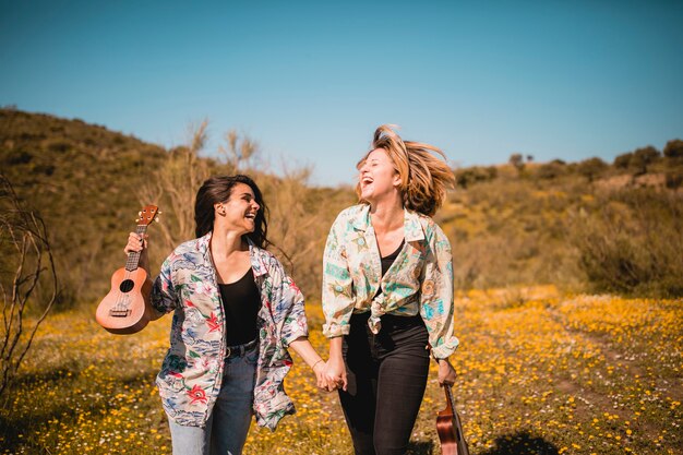 Cheerful women with ukuleles walking in field