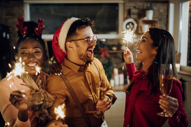 Cheerful young adults drinking champagne and using sparklers on New Year's party at home