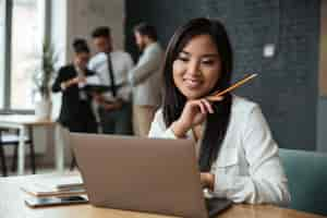 Free photo cheerful young asian businesswoman using laptop