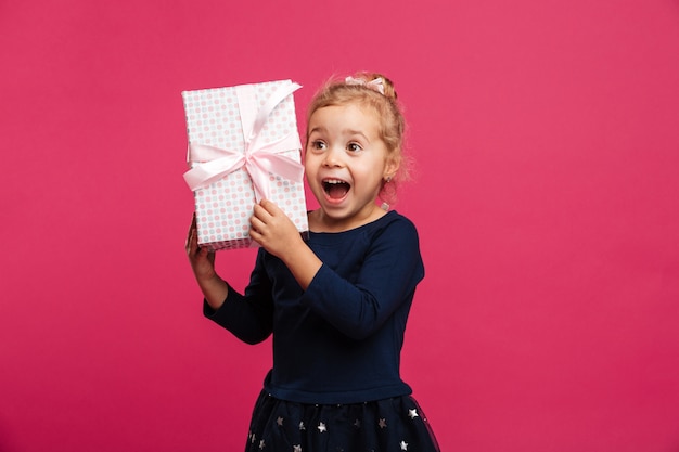 Cheerful young blonde girl holding gift box and rejoices