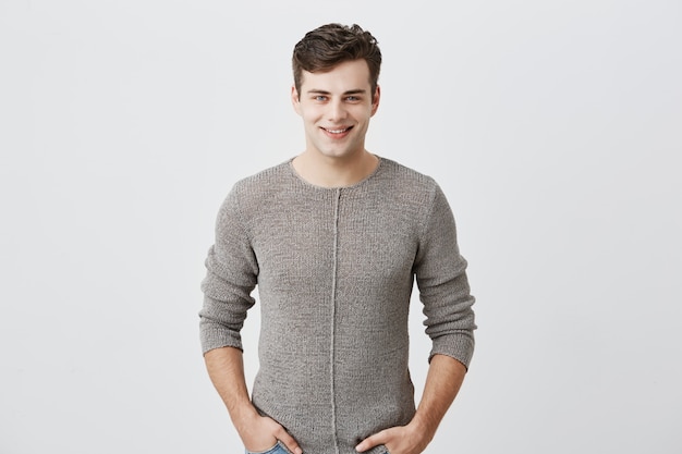 Free photo cheerful young blue-eyed man with dark hair posing in studio with happy smile, handsome fit man dressed casually smiling joyfully, showing his white straight teeth. positive emotions concept.