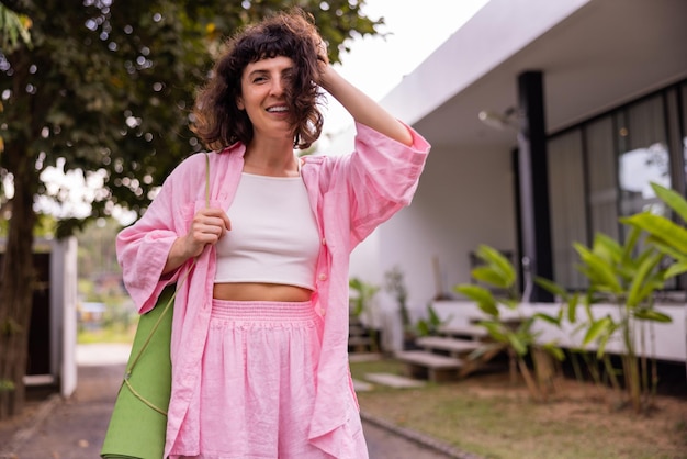 Cheerful young caucasian brunette woman in casual clothes smiling at camera while touching her hair outdoors Mood lifestyle concept