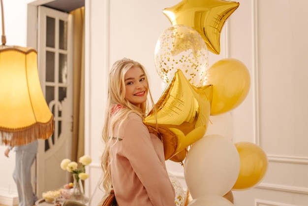 Cheerful young european blonde woman in high spirits posing with balloons at pajama party Holiday concept