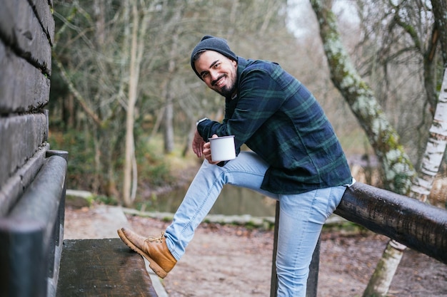 Free photo cheerful young hipster spending leisure time drinking coffee outdoors, autumn in the countr