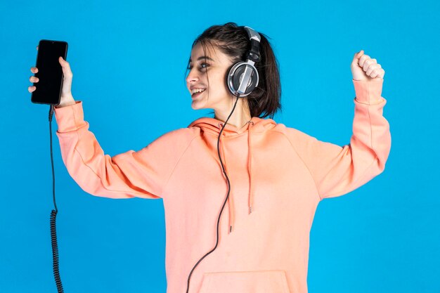 Free photo a cheerful young lady wearing headphones and looking at her phone