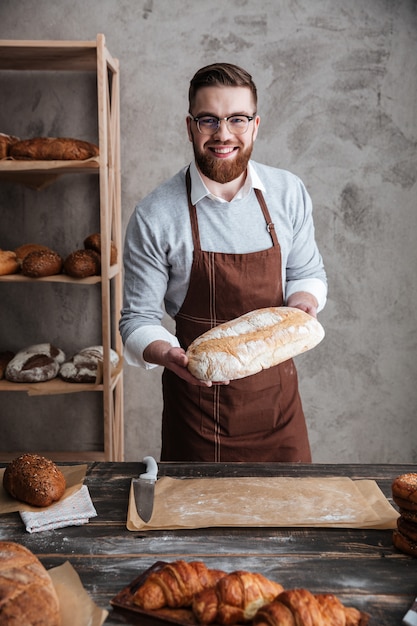 Cheerful young man baker standing at bakery holding bread