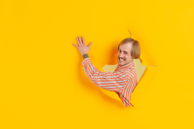 Free Photo cheerful young man poses in torn yellow paper hole wall emotional and expressive