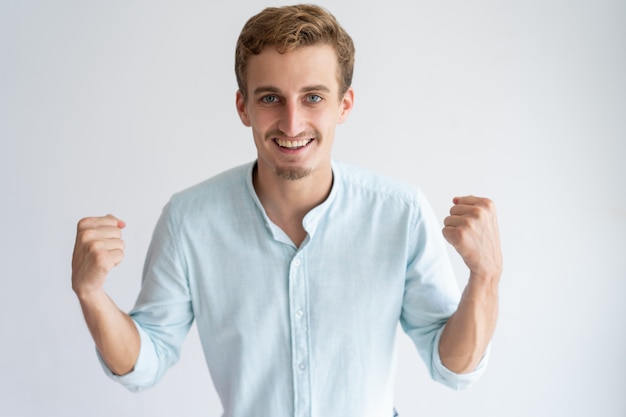 Cheerful young man pumping fists and looking at camera