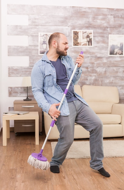 Cheerful young man singing and cleaning the house