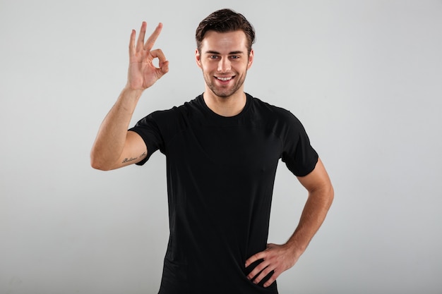 Cheerful young sports man posing showing ok gesture.