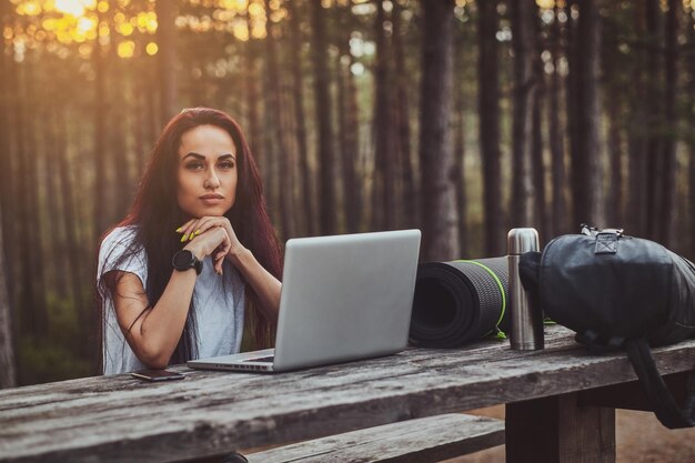 Cheerful young student is working on the laptop in the middle of the forest.