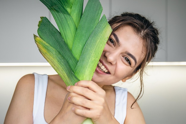 Free photo cheerful young woman in the kitchen holds a leek in her hands